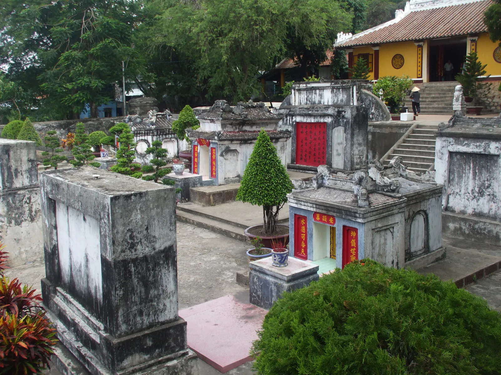 Khu lăng mộ cổ dưới chân Núi Sam ở Châu Đốc: các ngôi mộ xây vôi đá xám rêu với câu đối chữ Hán sơn đỏ, sân lát phẳng có bậc cấp thấp và chậu cây cảnh, phía sau là nhà thờ mái ngói tường vàng dựa lưng vào sườn đồi rậm cây